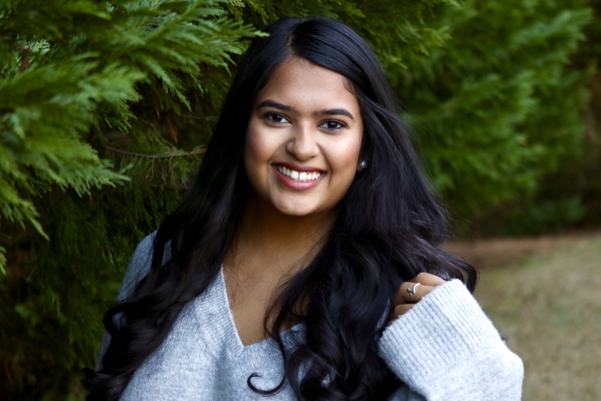 Woman wearing a white shirt and smiling in front of trees